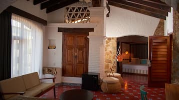 A cozy room with a sofa, ottoman, and a small table. There is a wooden door and a window with curtains.