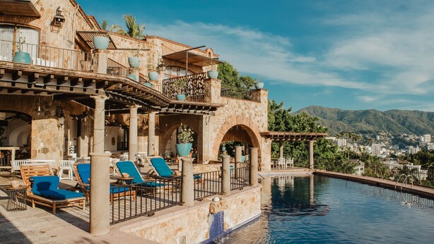 A poolside area with lounge chairs and a stone building with arches. - Casa Lisa by Hoteles BF (Acapulco)