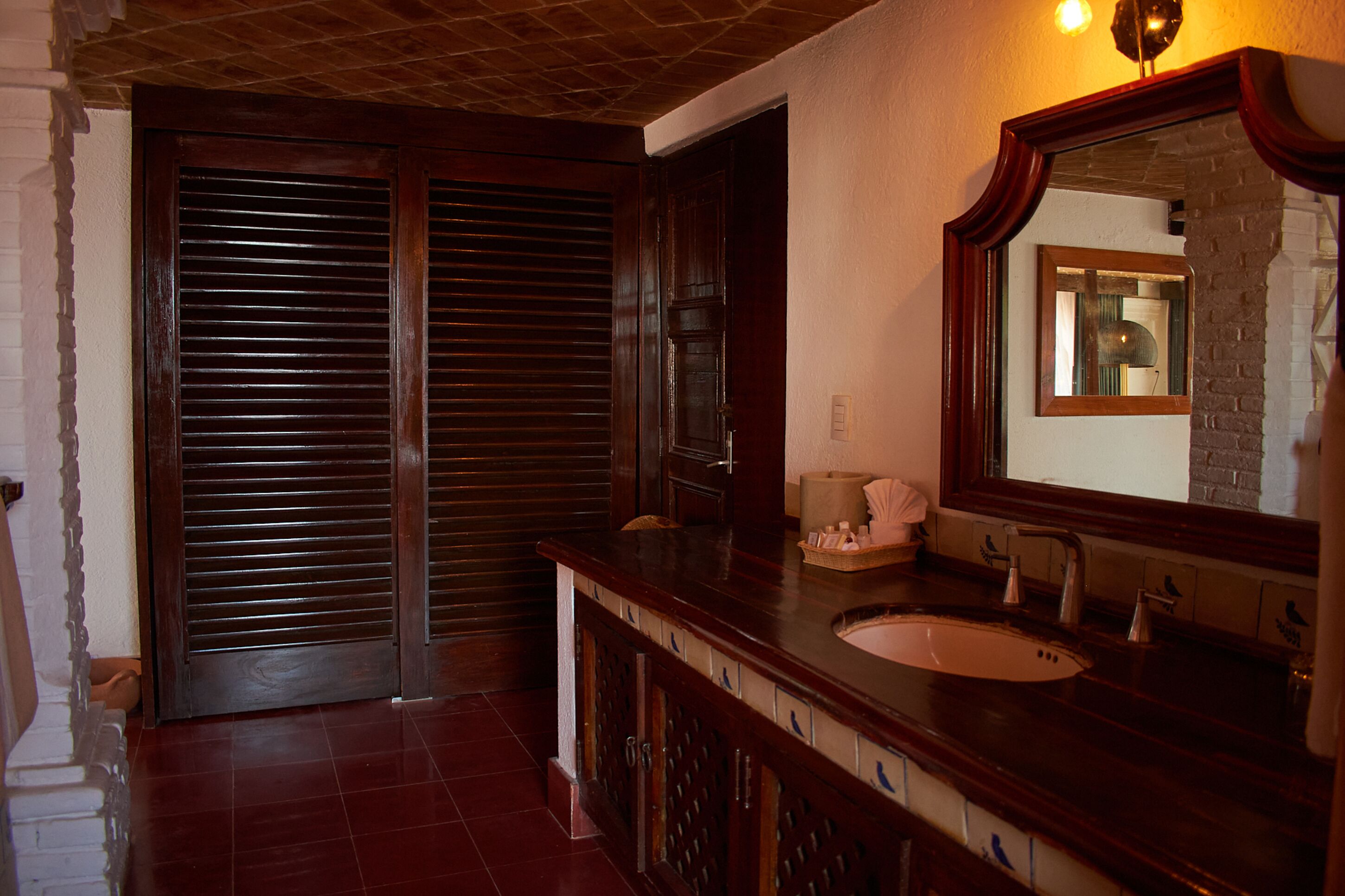 A bathroom with a wooden vanity, a sink, a mirror, and a door with horizontal louvered panels.