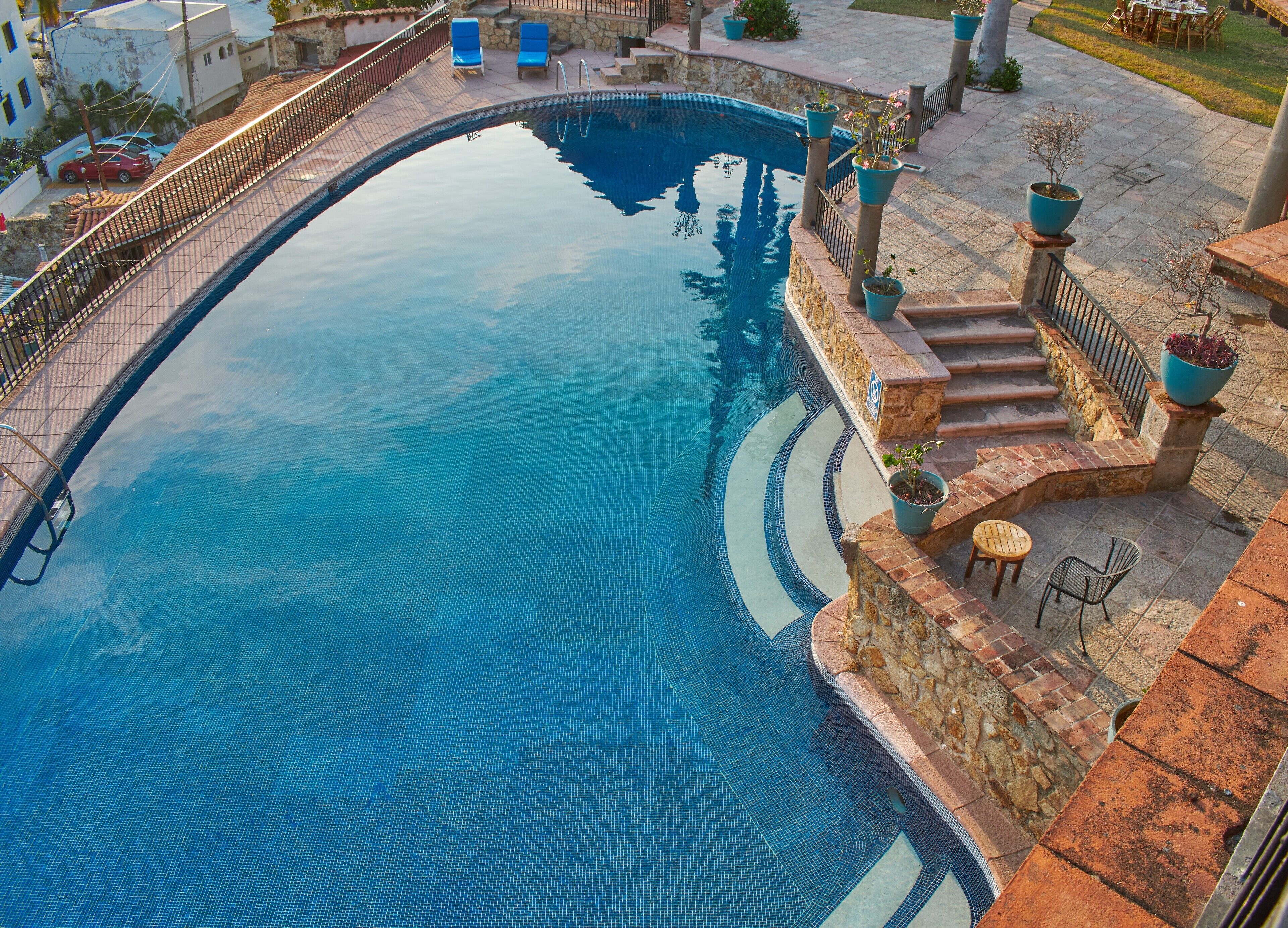 A swimming pool with a stone border, a small bridge, and outdoor seating.