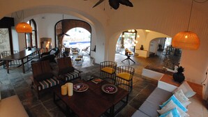 A spacious living area with a high ceiling, a dining table, multiple seating arrangements, and a view through an arched doorway. - Casa Lisa by Hoteles BF (Acapulco)