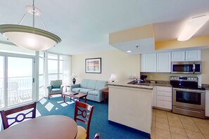 A compact living space with a dining area, a sofa, a small kitchen with a microwave and stove, and a balcony with chairs. - Carolinian Beach Resort by Vacasa (Myrtle Beach)