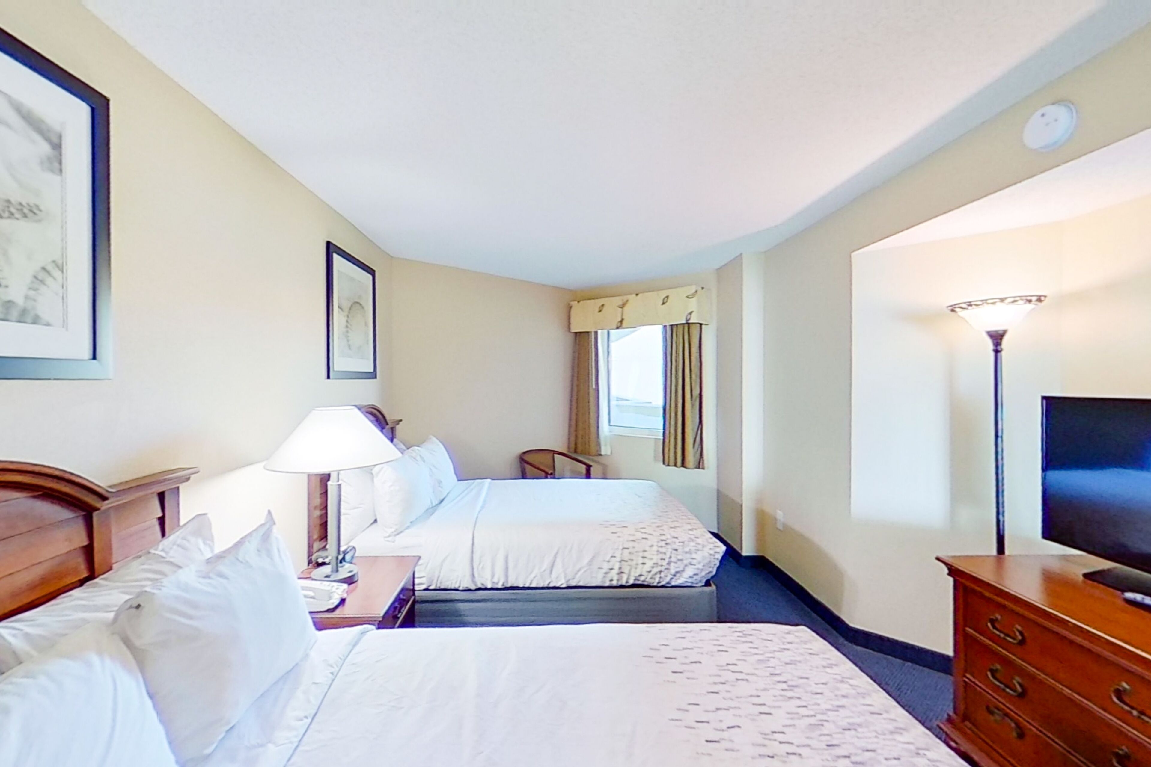 A hotel room with two beds, a TV, a lamp, and a dresser.