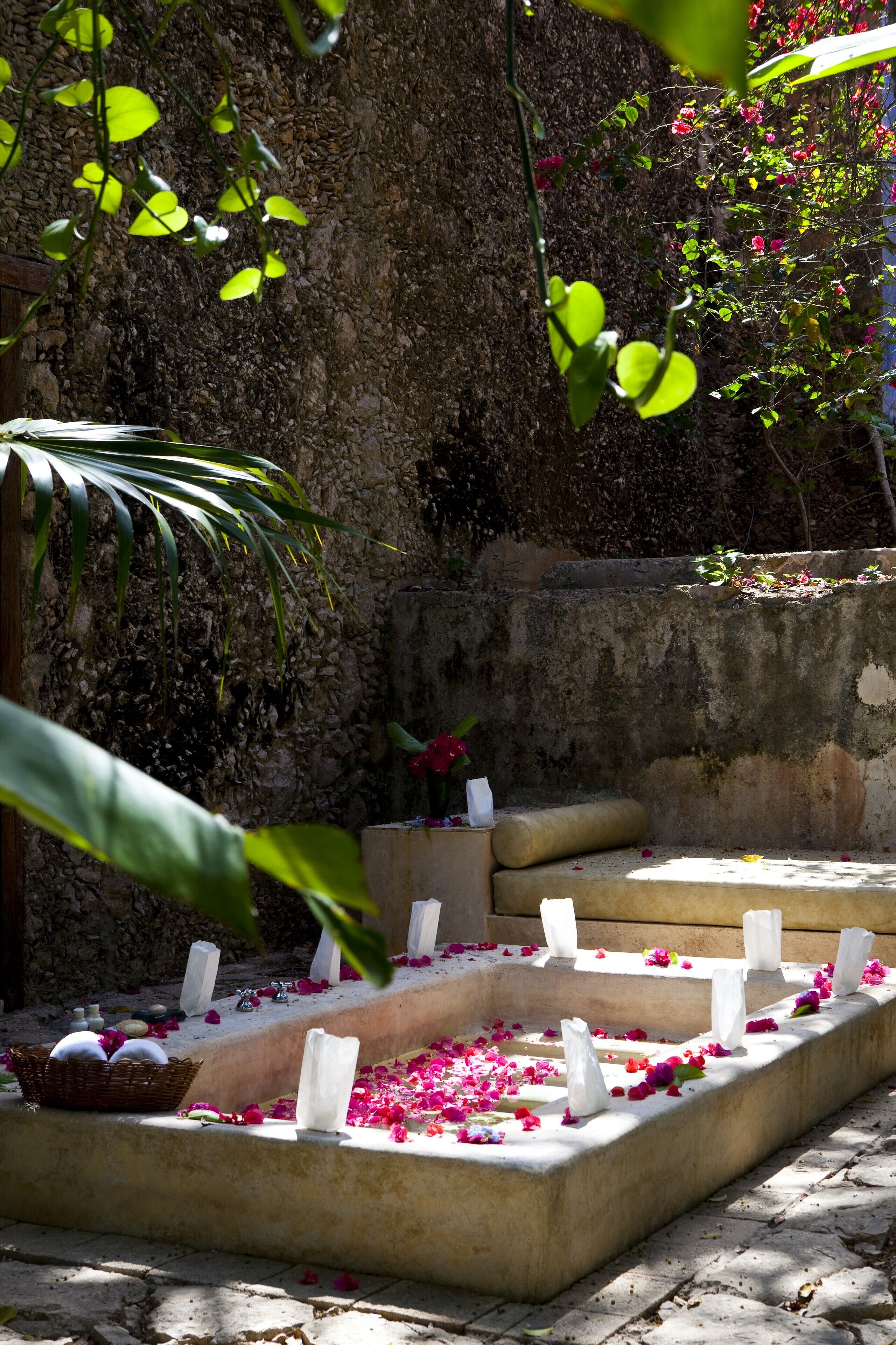 A stone bench with white candles and scattered rose petals.