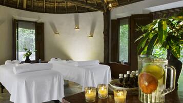Et spa-rum med to massagestole, stearinlys, en drik tilsat frugt og udsigt til grøn vegetation.