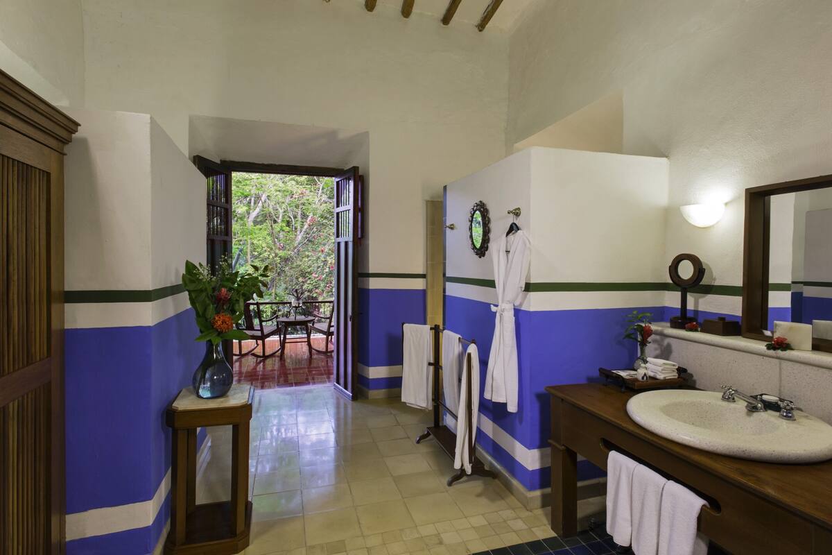 Baño con un lavamanos grande, un espejo y un perchero. Hay una puerta que da a un espacio exterior con una mesa y sillas.