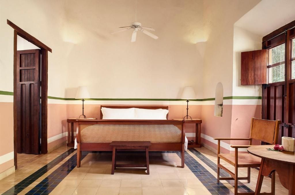 A room with a bed, a table, a chair, a ceiling fan, and a window.