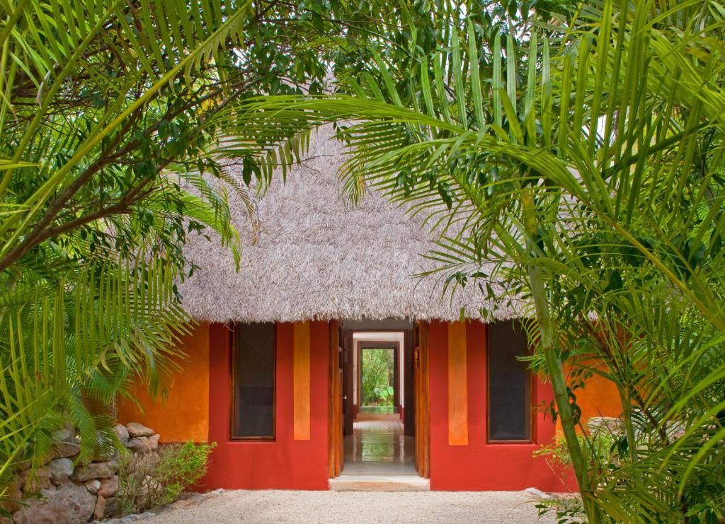 A thatched-roof structure with a red facade and a pathway leading to a door.
