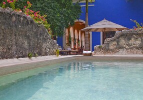 Una piscina cristalina con un área de descanso, que incluye una mesa y sillas, y una sombrilla.