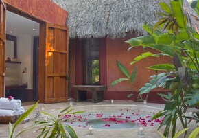 Un área de spa con techo de paja, una bañera de hidromasaje de piedra y un banco de madera.