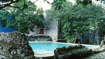 Un patio con piscina, muros de piedra y abundante vegetación.