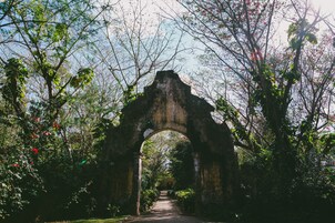 Una estructura de piedra arqueada en un jardín con un sendero que la atraviesa.