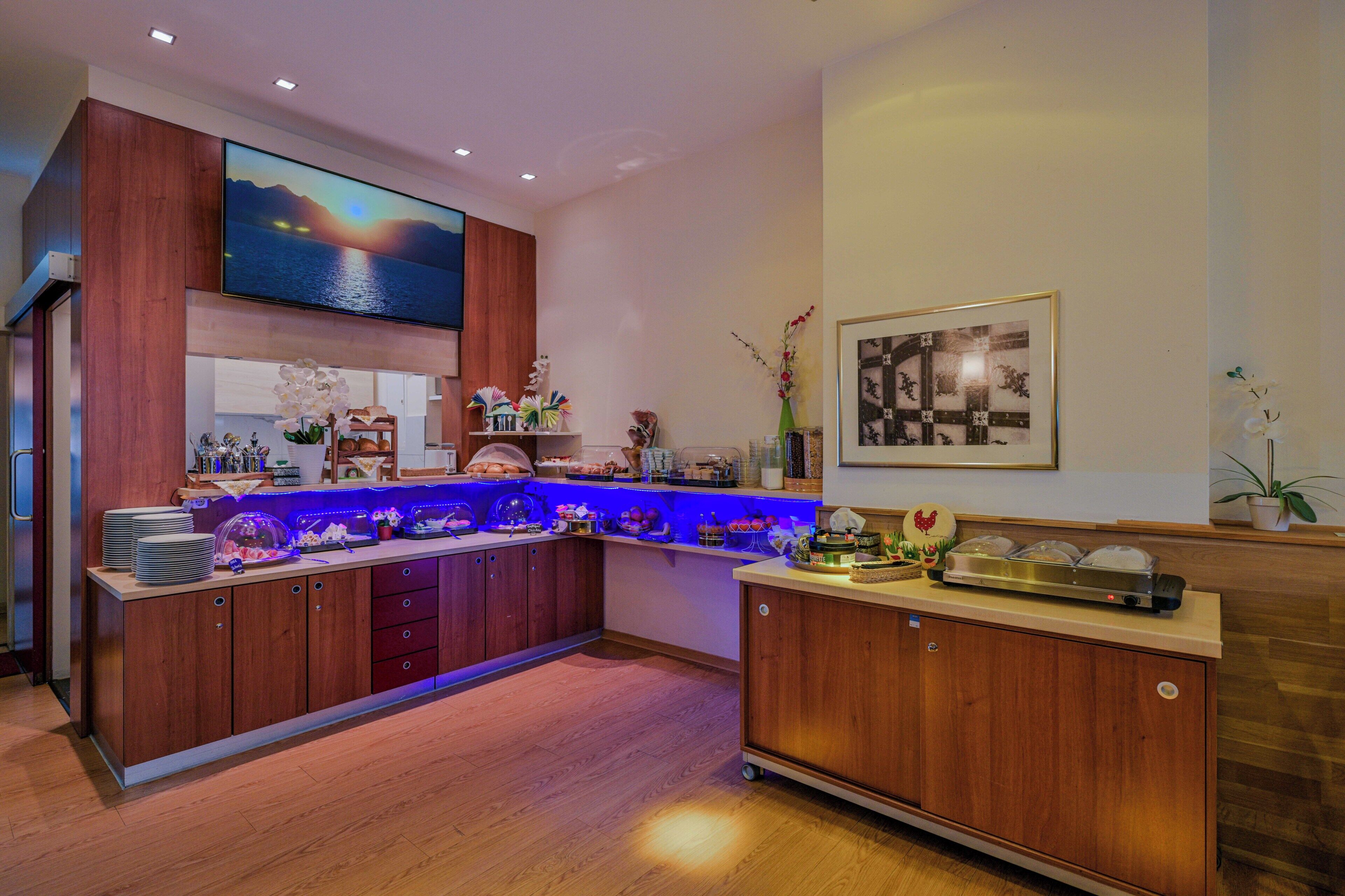 Una cuina moderna amb armaris de fusta, una zona de bar amb il·luminació blava, un televisor de pantalla plana gran i un quadre encadrejat a la paret.