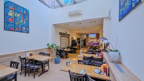 A restaurant with wooden tables and chairs, potted plants, and a stained glass window. - Hotel Münchner Hof (Frankfurt)