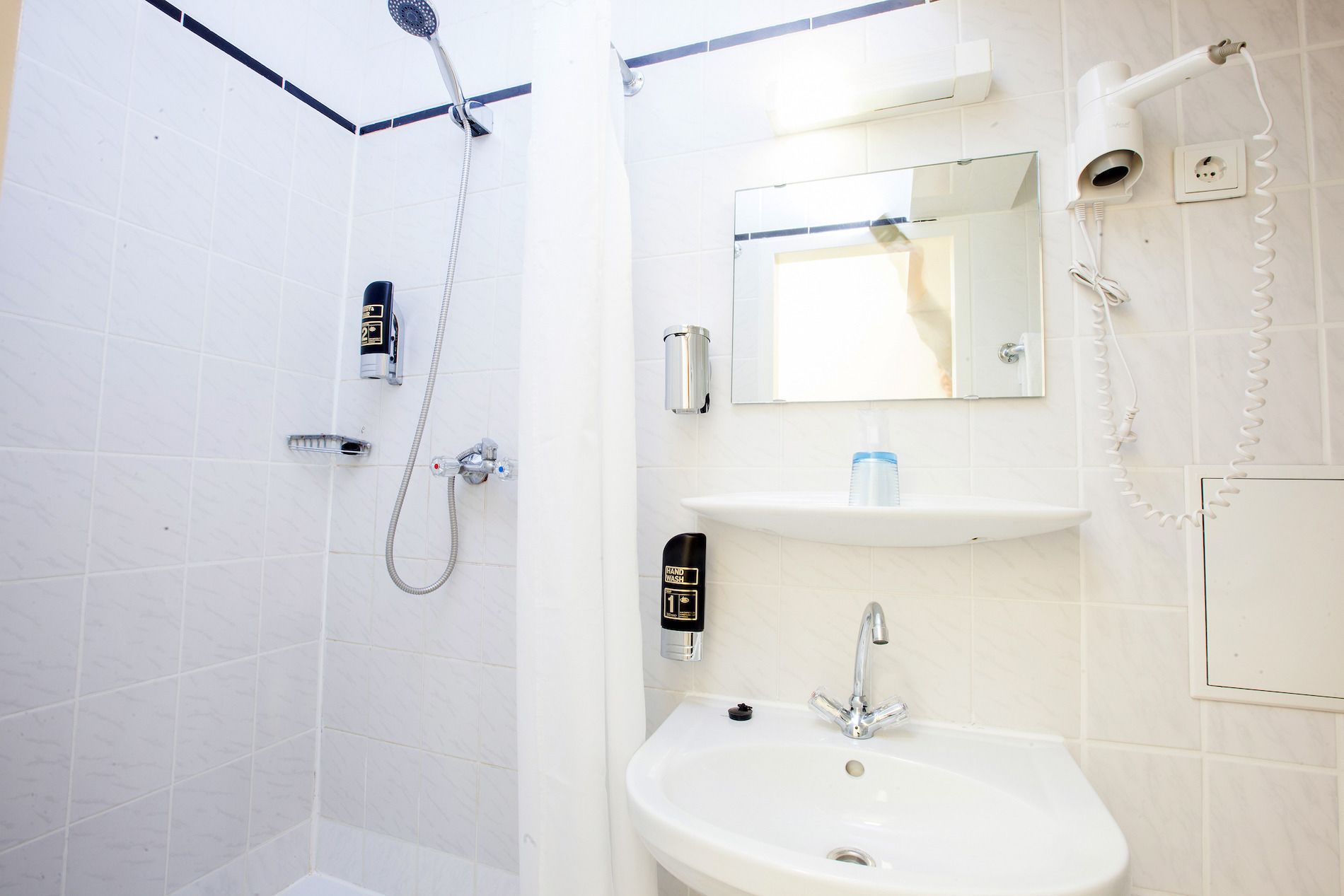 Un baño con ducha, lavabo, espejo y secador de manos.