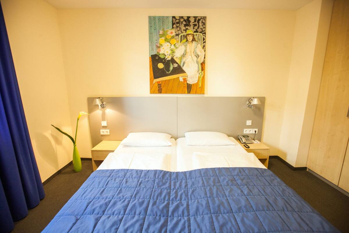 A hotel room with a large bed, two bedside tables, a painting above the bed, and a telephone on one of the tables.