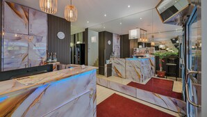 A hotel reception area with marble counters, modern pendant lighting, a clock, and a view of the interior through a glass wall. - Hotel Münchner Hof (Frankfurt)