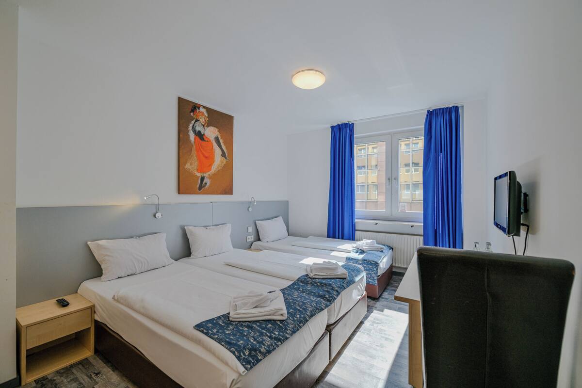 A hotel room with two beds, a desk, a chair, a television, and a painting on the wall.