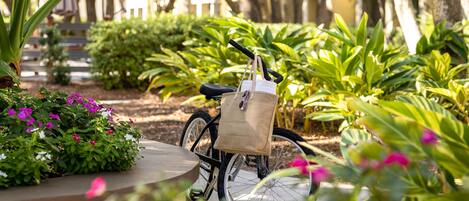 A bicycle with a bag attached to the back, parked in a garden with various plants and a wooden fence in the background.