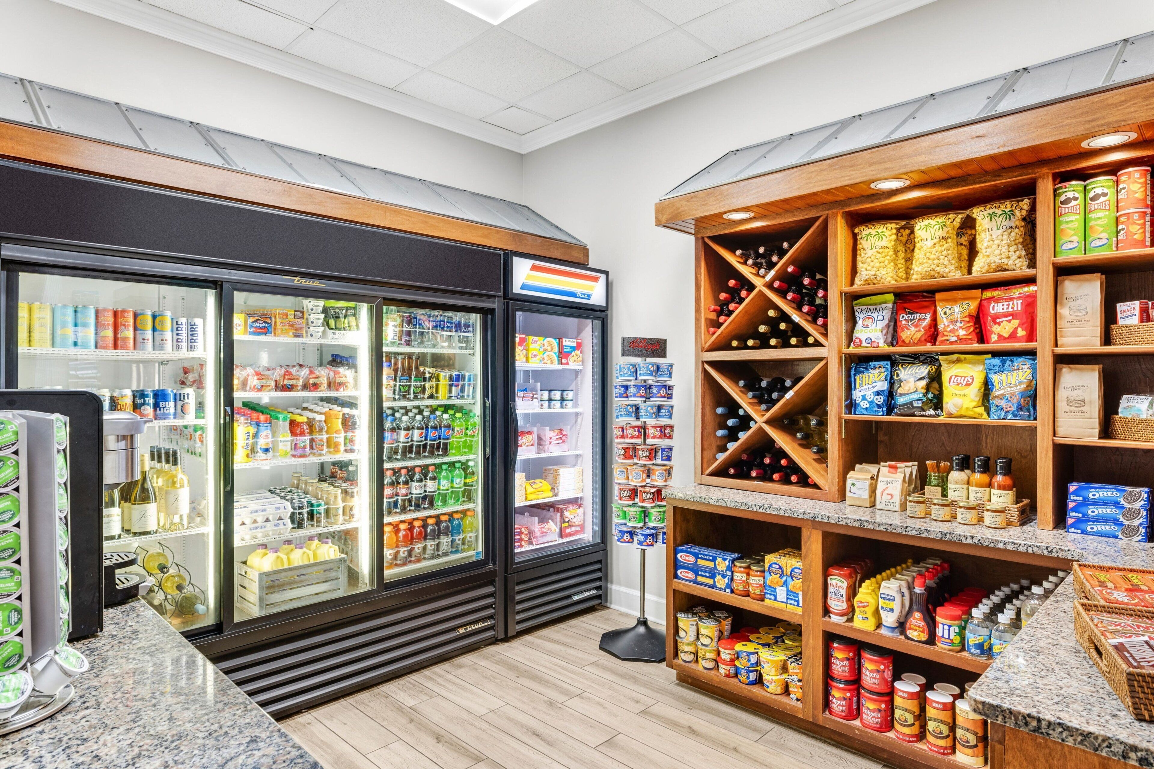 Interior de una tienda de comestibles con secciones refrigeradas, estantes llenos de refrigerios y una estación de bebidas de autoservicio.