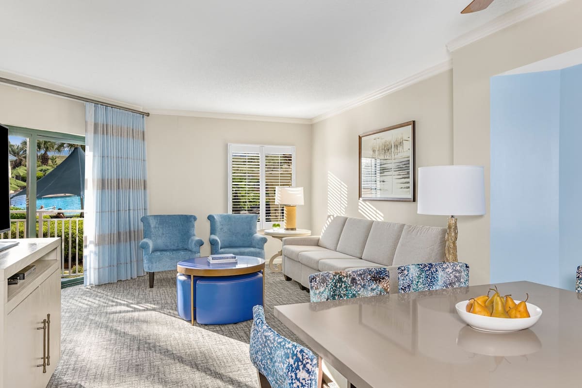 A modern living room with a sofa, armchairs, a coffee table, and a dining table with a fruit bowl.