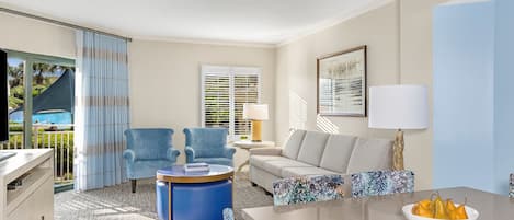 A modern living room with a sofa, armchairs, a coffee table, and a dining table with a fruit bowl.
