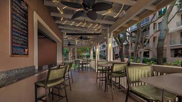 A covered outdoor seating area with tables and chairs, ceiling fans, and a menu board on the wall.
