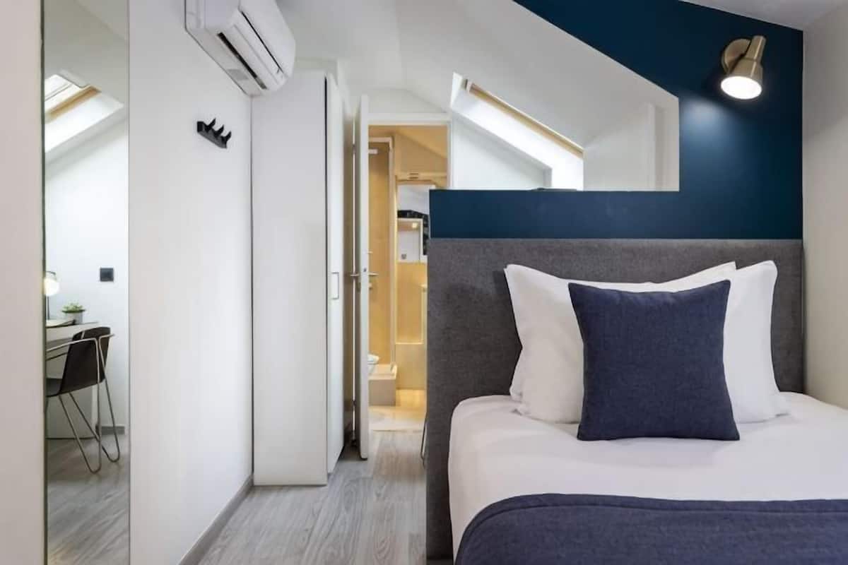 Une chambre d’hôtel avec un lit, un bureau et une salle de bain, visibles à travers une porte ouverte.