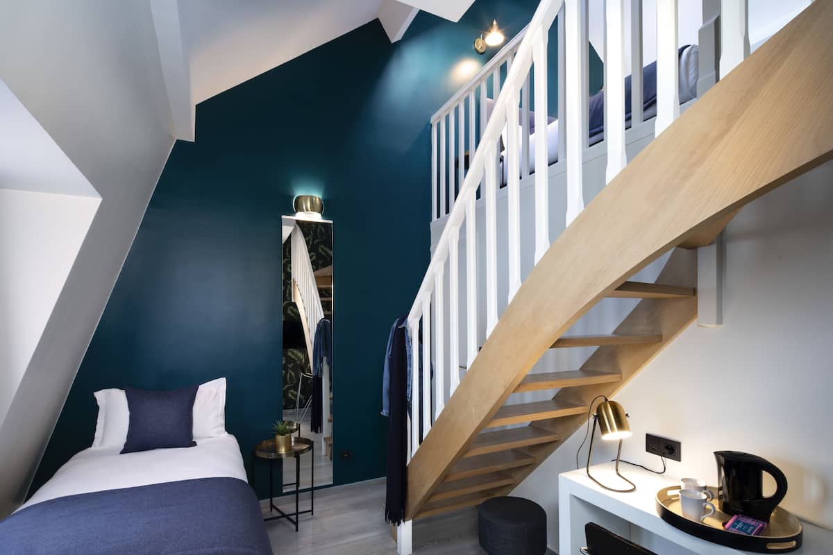 Une chambre moderne avec un lit, un bureau doté d’une lampe et un escalier.