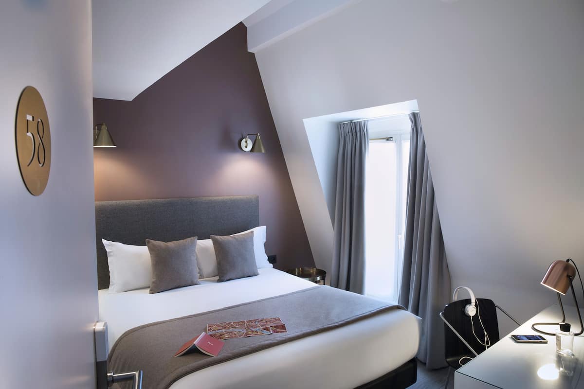 Une chambre d’hôtel moderne avec un grand lit, un bureau avec une lampe et une vue sur l’extérieur.