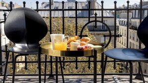 Een balkon met een ontbijttafel, twee stoelen en uitzicht op gebouwen.