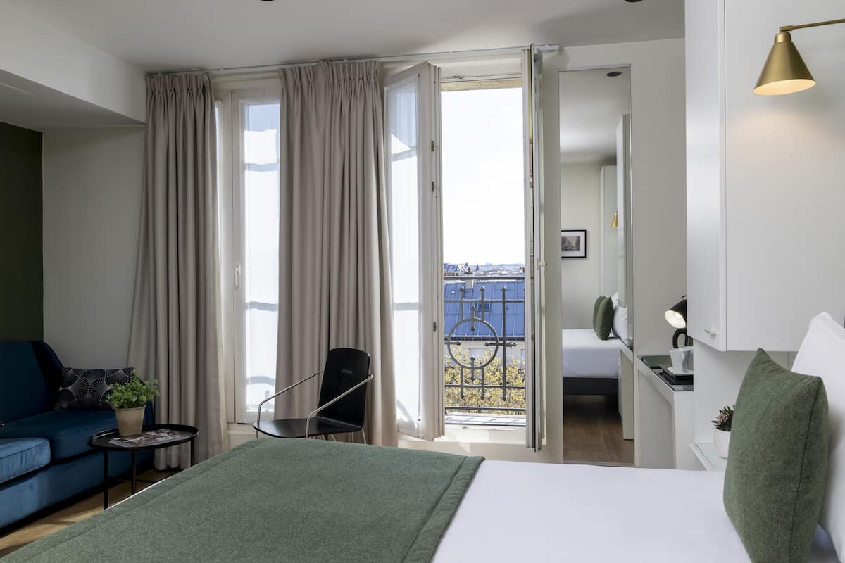 Une chambre d’hôtel moderne équipée d’un lit, d’un bureau, d’une chaise, d’un canapé et d’un balcon avec vue.