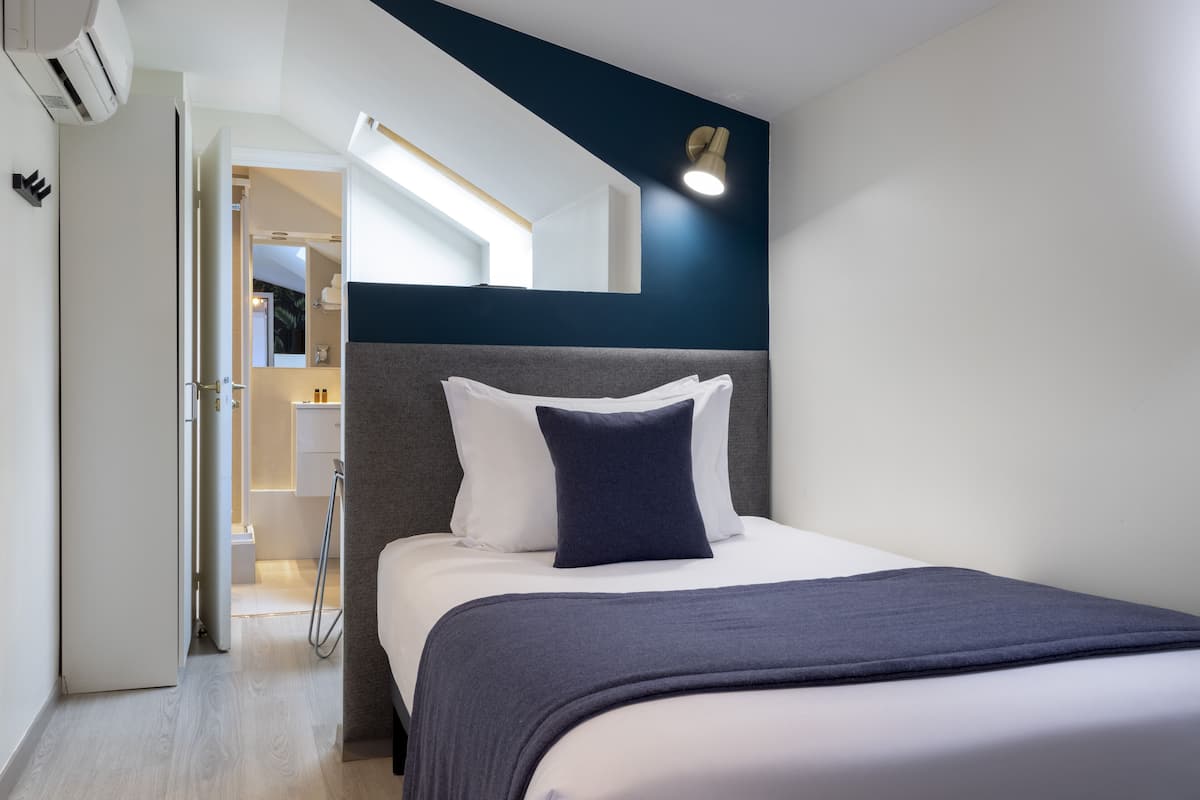 Une chambre d’hôtel moderne avec un lit bien fait, un dressing et une lucarne au-dessus du lit.