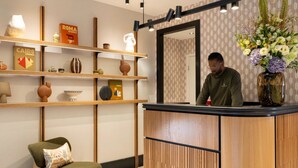 Een receptiezone met een houten balie, planken met decoratieve objecten, een stoel en een spiegel.