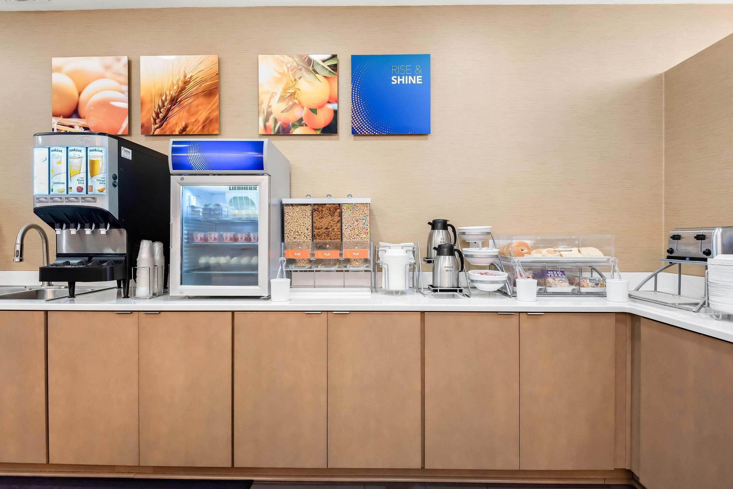 Un espace de petit-déjeuner en libre-service comprenant une machine à café, un présentoir réfrigéré et divers choix de produits alimentaires.