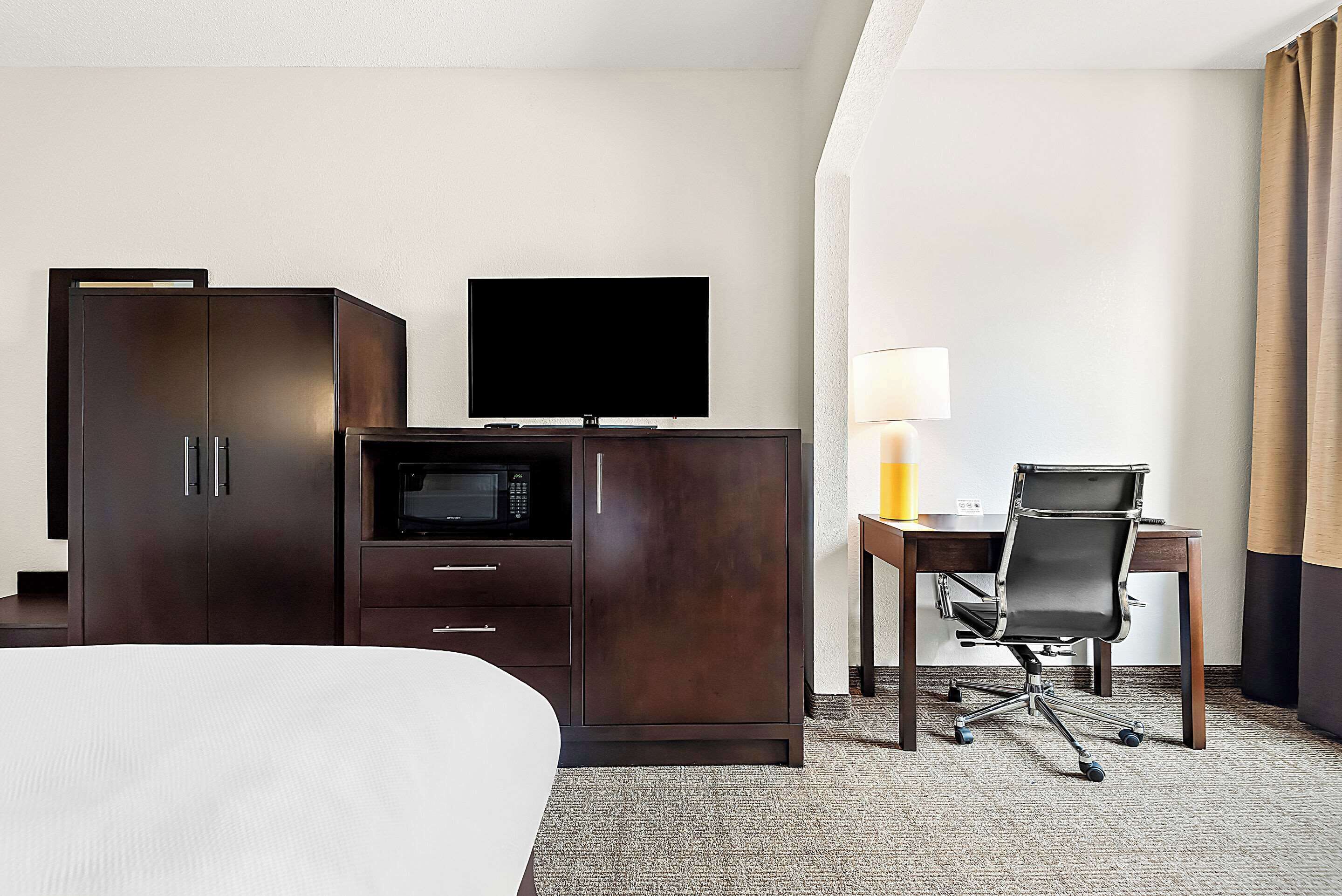 Habitación de hotel con cama, armario, escritorio con silla, televisor de pantalla plana y microondas.