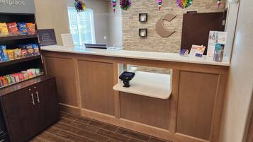 A reception area with a counter, a coffee machine, a shelf with snacks, and a wall clock.