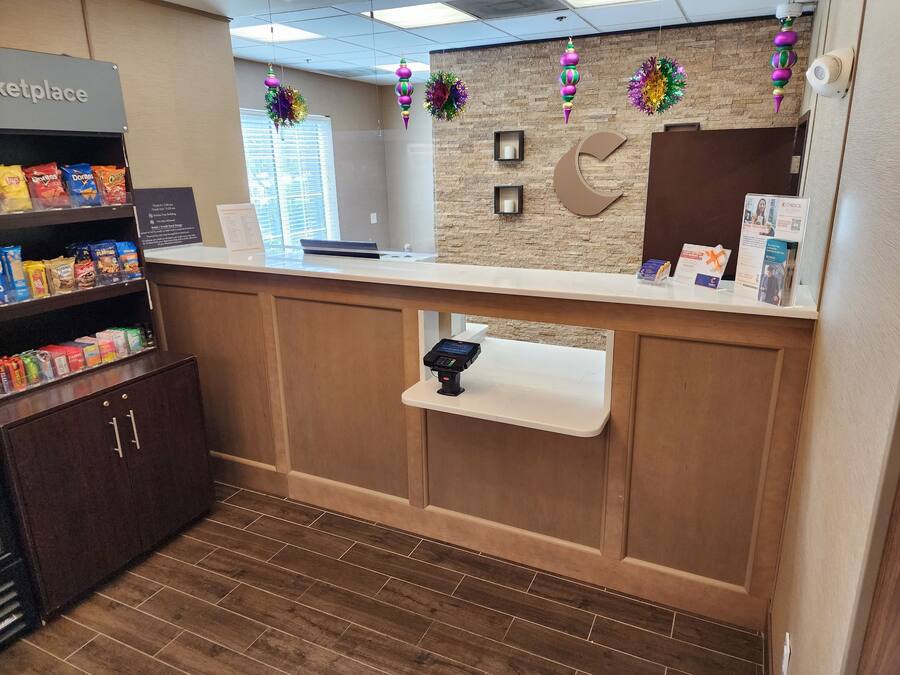 A reception area with a counter, a coffee machine, a shelf with snacks, and a wall clock.