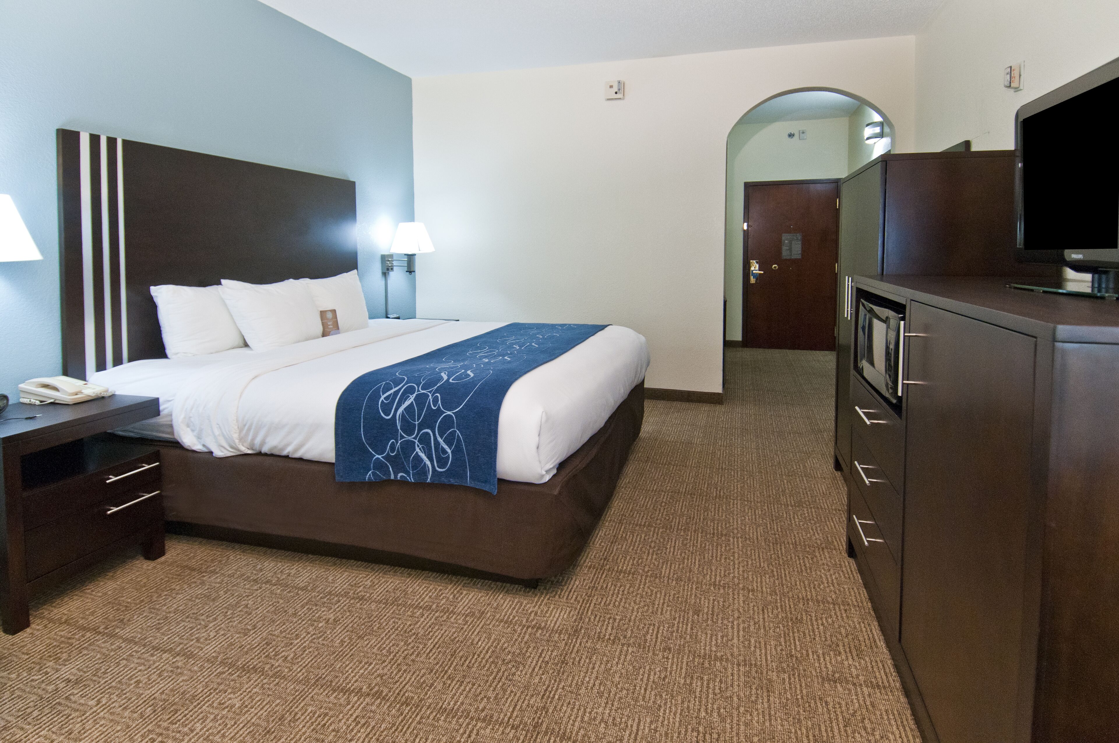Une chambre d’hôtel comprenant un lit, des lampes de chevet, un bureau avec un téléphone, une télévision et une armoire.