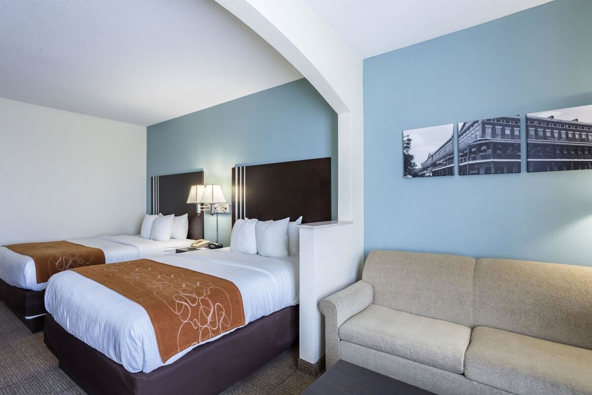 A hotel room with two beds, a sofa, a lamp, and a wall-mounted picture.