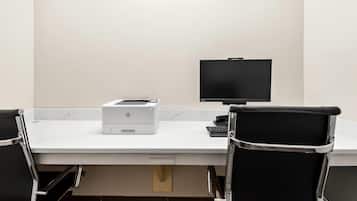 A conference room with a white table, two black office chairs, a printer, and a monitor.