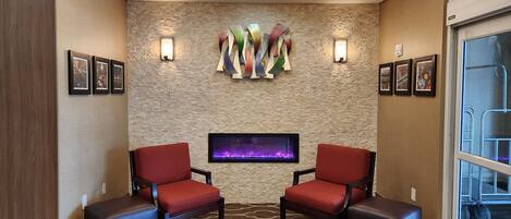 A lobby with a stone wall, two red chairs, a flat-screen TV, and a ceiling light fixture.