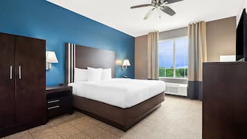 Une chambre d’hôtel avec un grand lit, une armoire en bois sombre, des tables de chevet avec des lampes, un ventilateur de plafond et une grande fenêtre avec des rideaux.