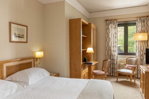 A hotel room with a large bed, a desk with a lamp, a chair, and a wardrobe.