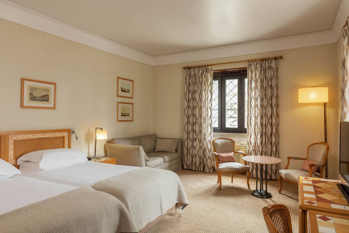 Una habitación de hotel con dos camas, un sofá, una mesita, una silla y un televisor.