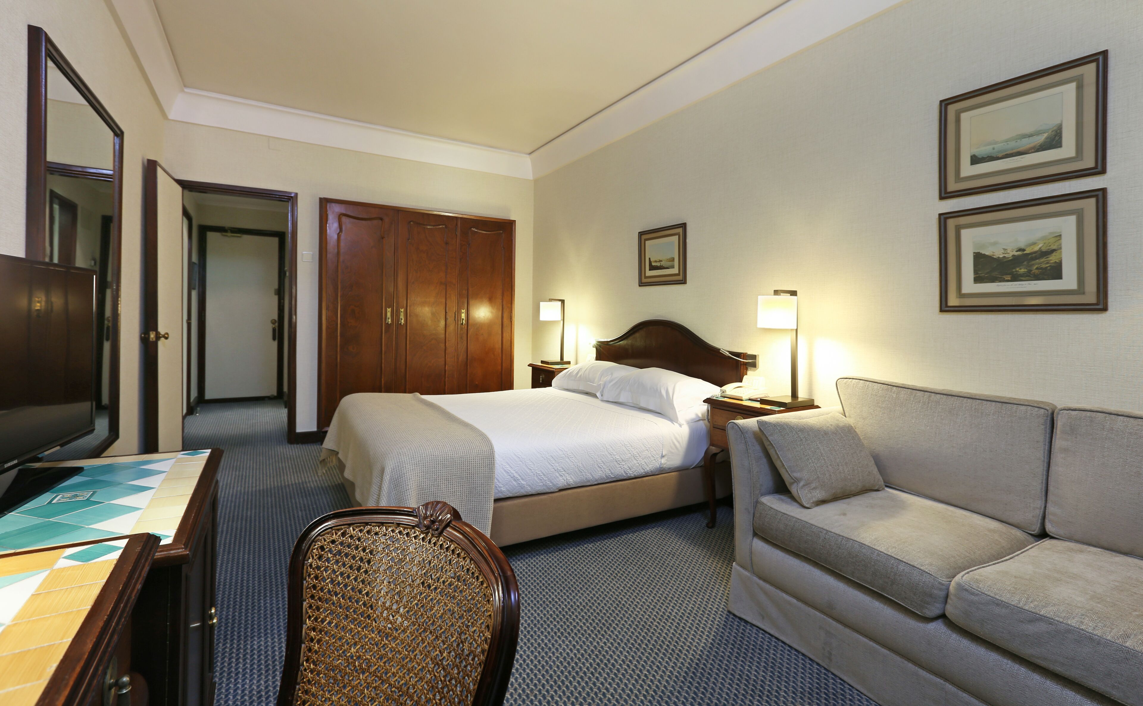 Quarto de hotel com uma cama, sofá, escrivaninha e televisão.