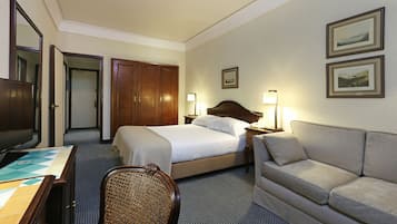 Quarto de hotel com uma cama, sofá, escrivaninha e televisão.