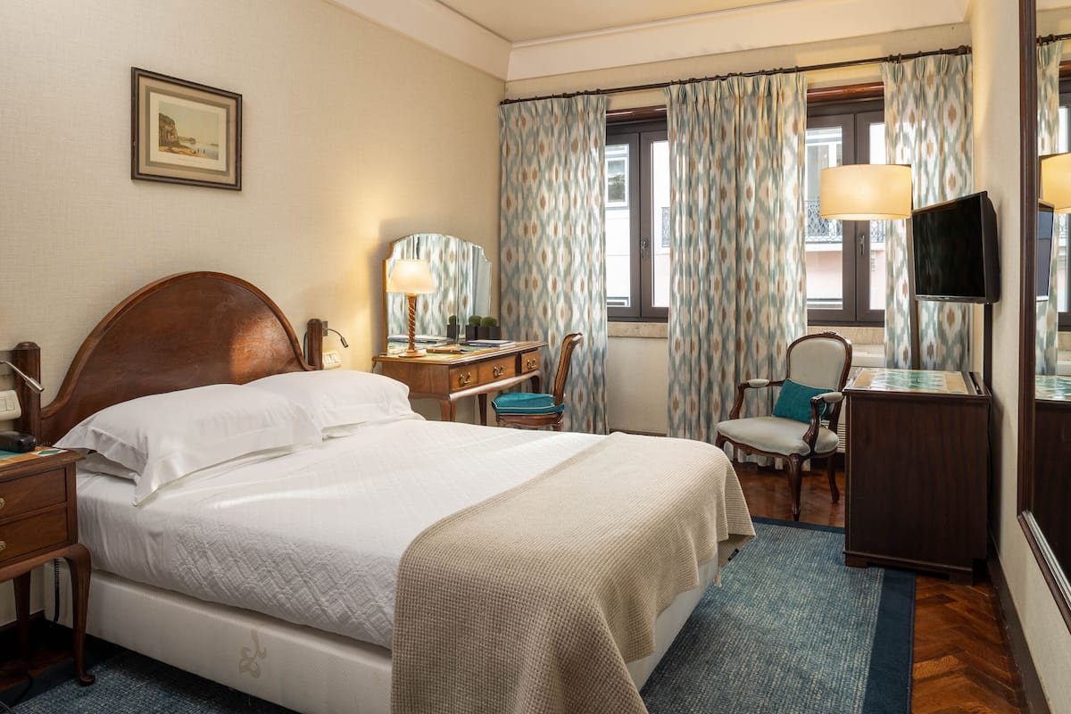 Una habitación de hotel con una cama grande, un escritorio con lámpara, una silla, un televisor y cortinas.