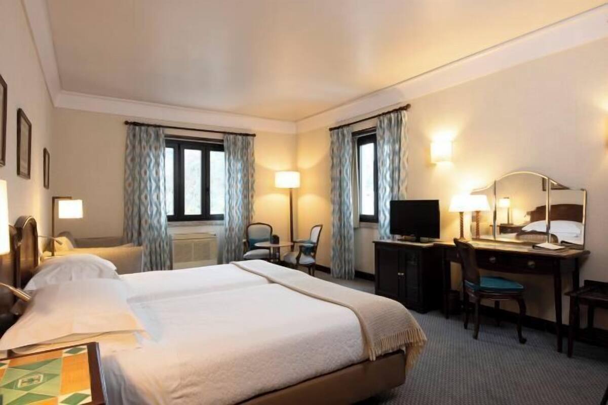 Una habitación de hotel con una cama grande, un escritorio, dos sillas, un televisor y un espejo.