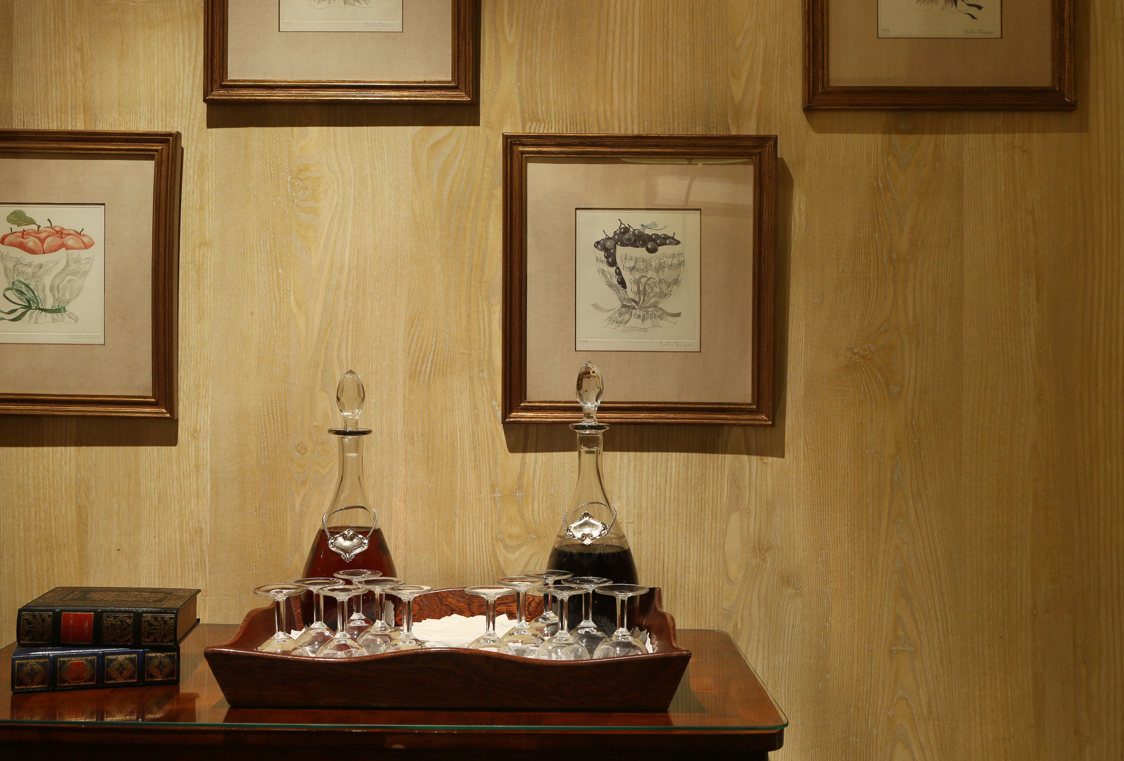 A wooden wall with framed artwork and a table with wine glasses and a decanter.